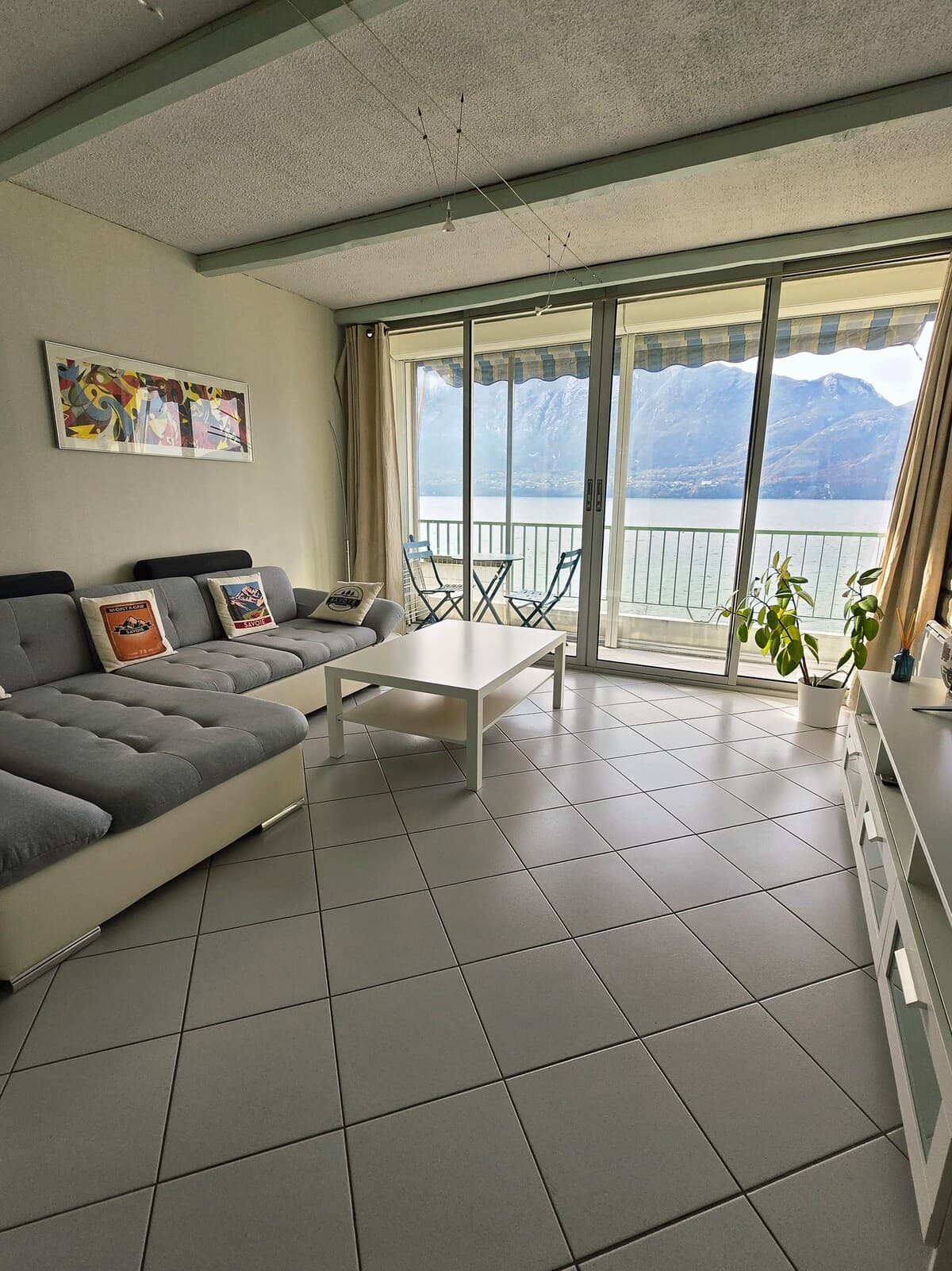 Séjour avec canapé d’angle, baie vitrée sur le balcon et vue sur le lac