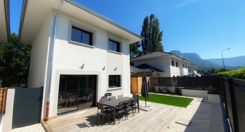 Maison côté jardin : terrasse en bois avec table et chaises, pelouse